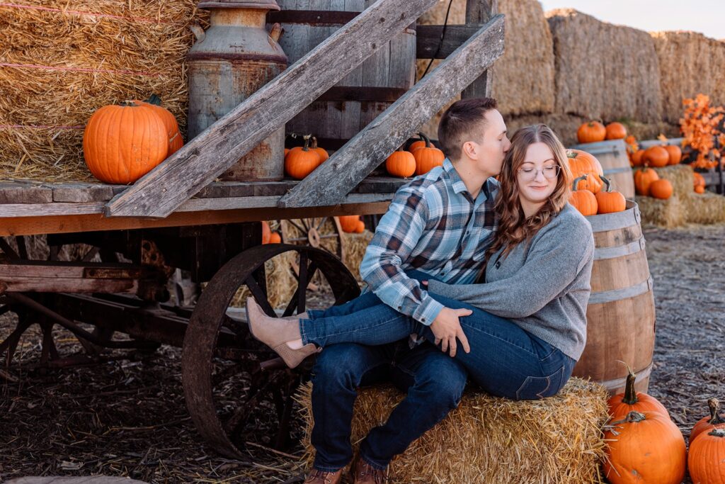 Couple sitting on a haybale in front of a wagon at a pumpkin patch