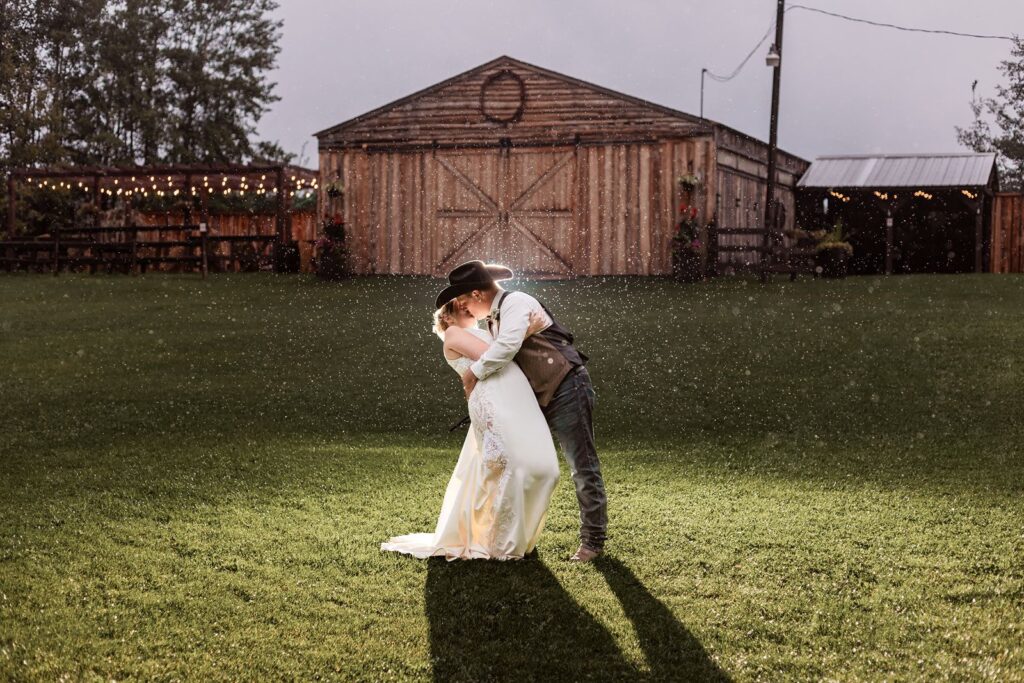 Groom dips his bride and kisses her in the rain in front of the reception venue at The Woven Willow