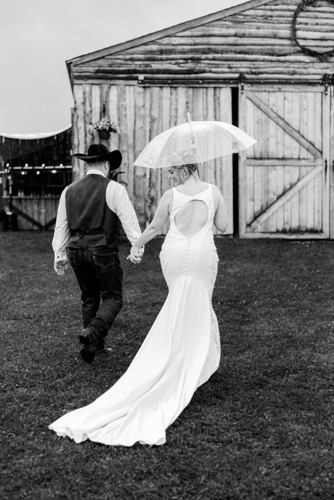 Bride and groom walk away from their ceremony in the rain holding hands