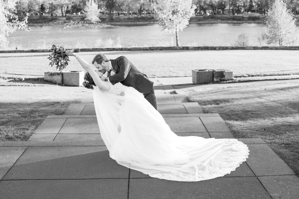 Groom dips and kisses bride in front of the river at Baker Park