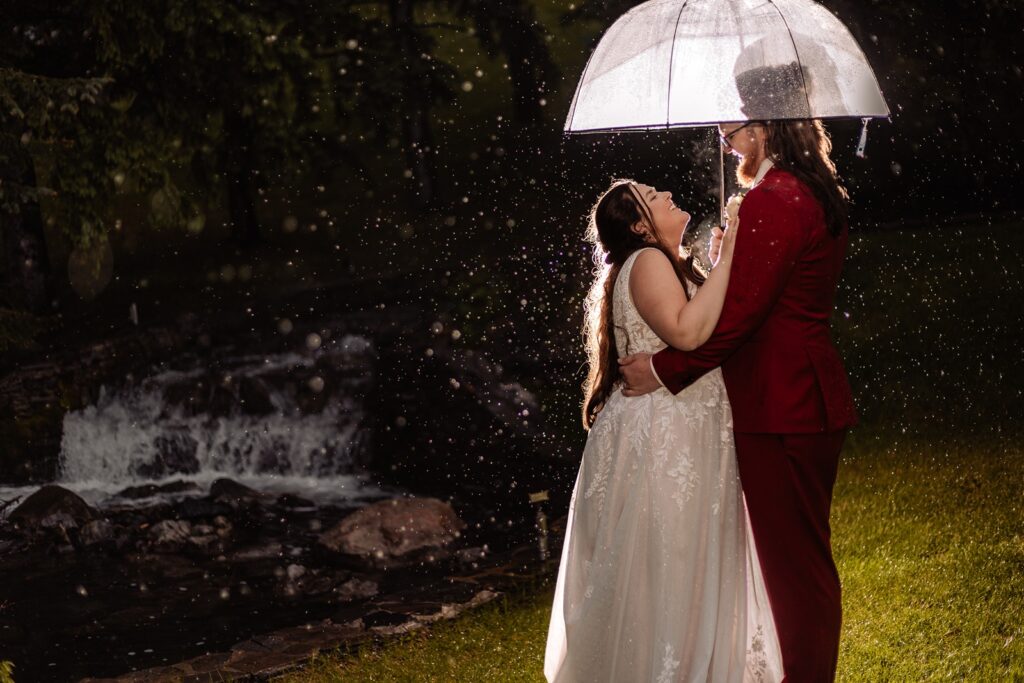 Bride and groom under a clear umbrella on their rainy wedding day