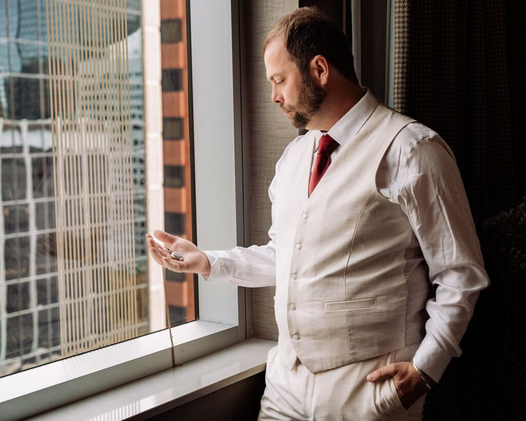 Groom looking at pocketwatch in front of a window at the Dorian hotel in Calgary