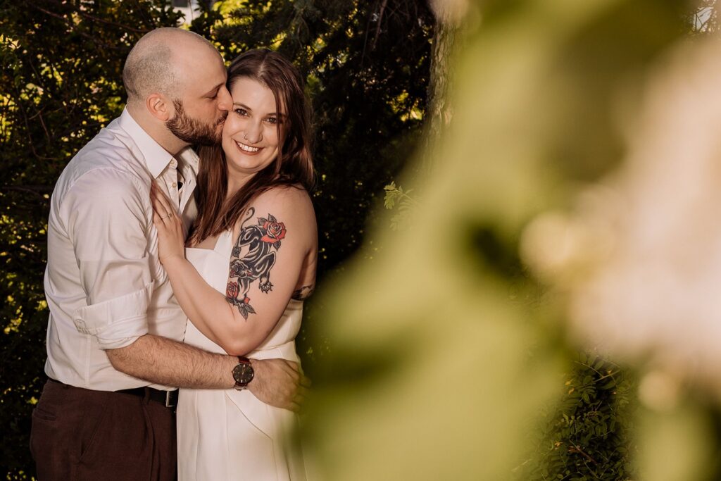 Man kissing fiance with foliage framing the right side of the image