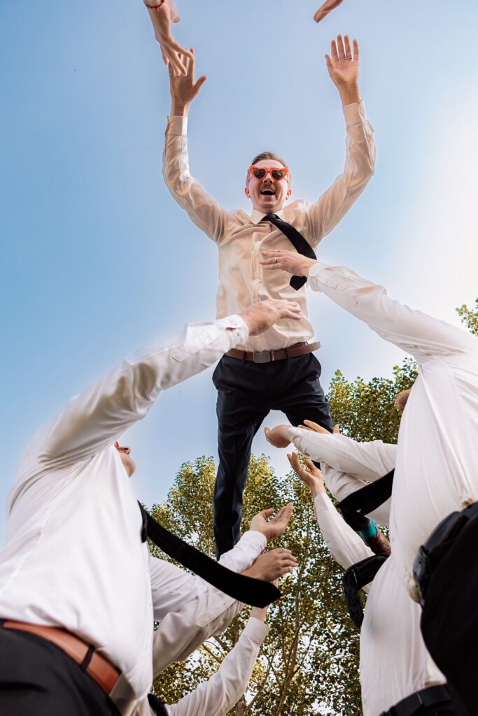 Groom being thrown into the air by his groomsmen